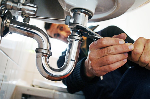 Close-up of plumber repairing sink. Male worker using tool while fixing appliance in bathroom. He is working on metallic equipment at home